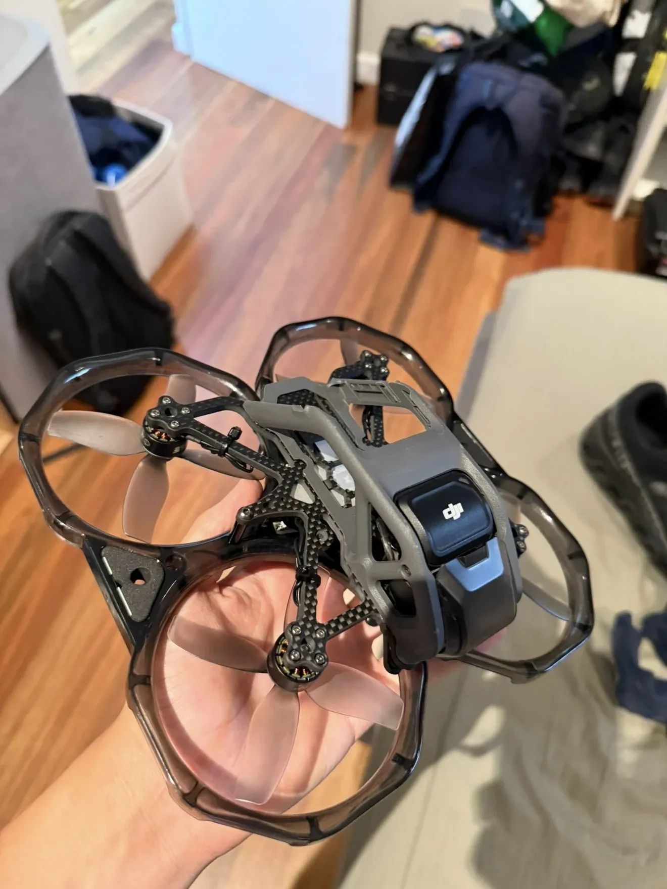 A modified DJI Avata held in one hand, with grey propeller guards and a carbon fibre frame around the DJI camera unit.