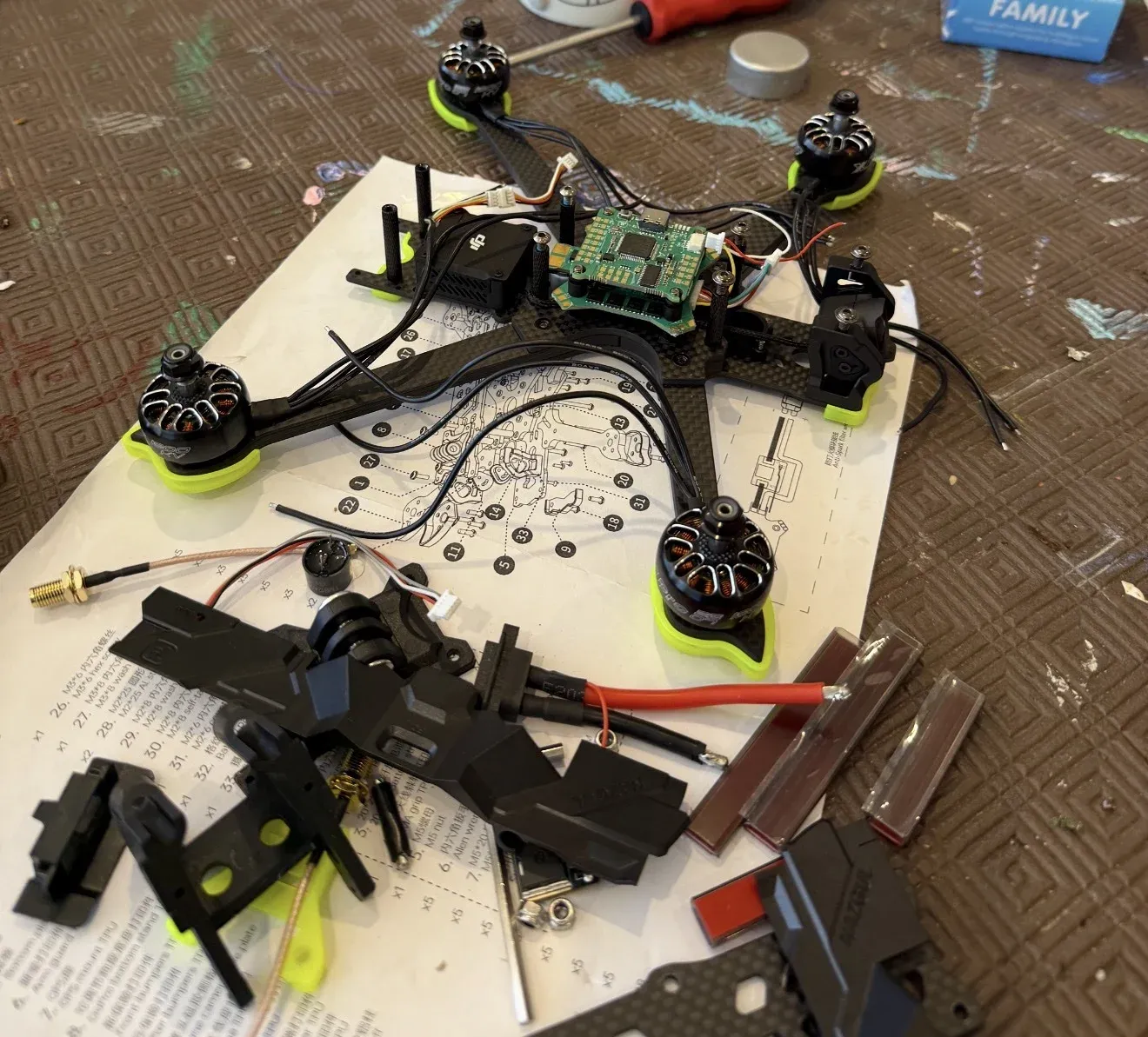 The FPV drone partly assembled on a workbench, with motors on green mounts, the flight controller in the middle, wiring, and spare parts around it.