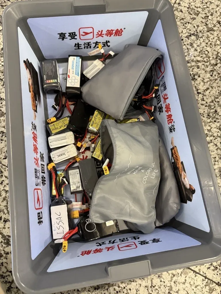 An airport security tray full of drone batteries in bags, with chargers and cables.
