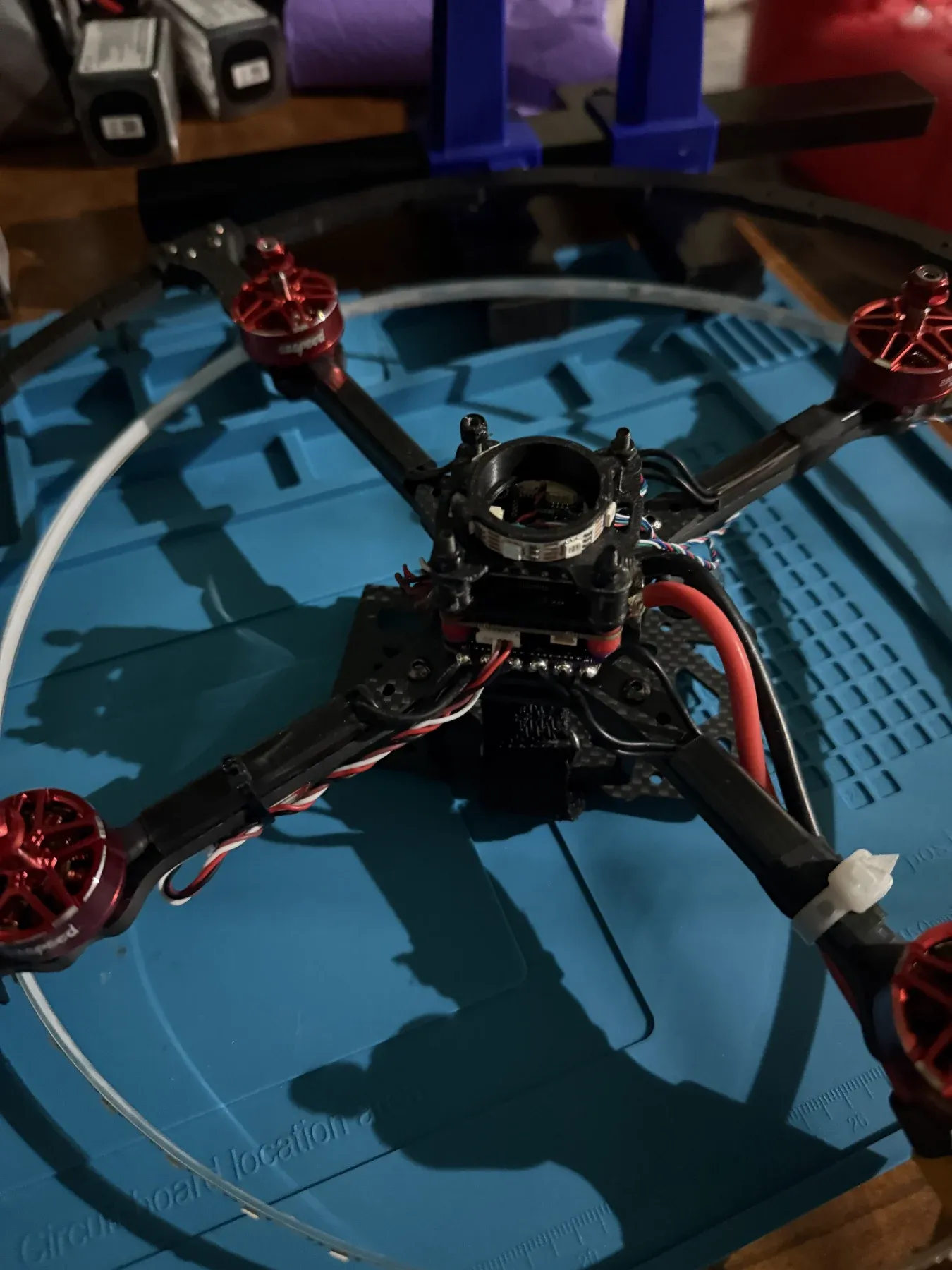A drone soccer drone with four red motors on a black frame inside its protective ball cage, sitting on a blue mat.