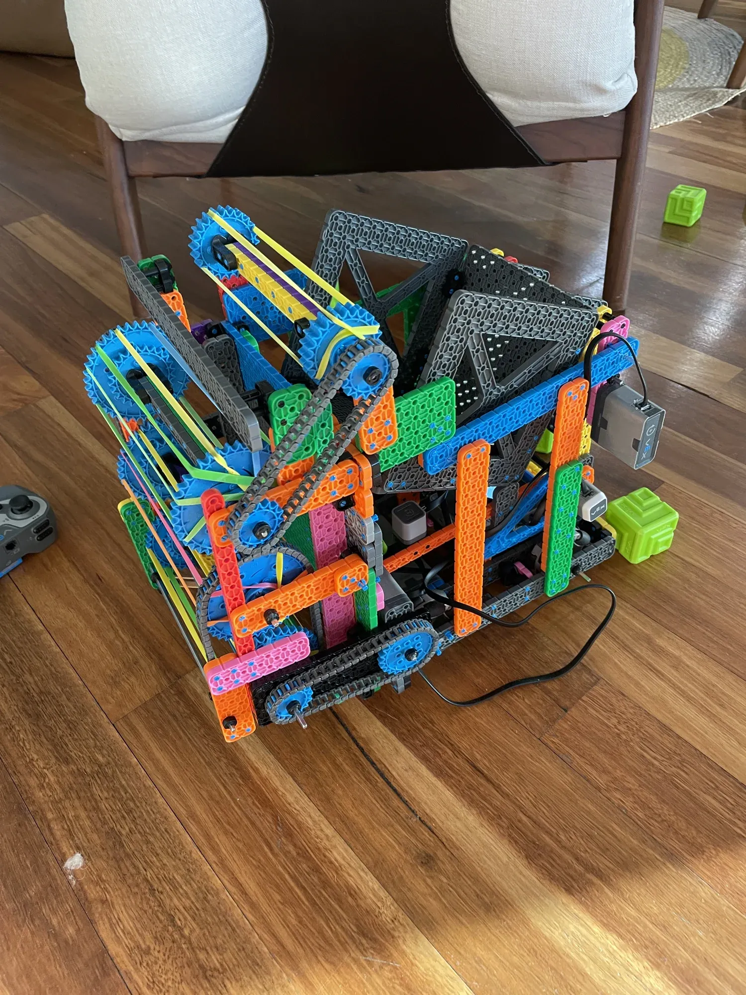 A colourful VEX IQ robot with orange, blue and green beams, with green Full Volume blocks beside it.