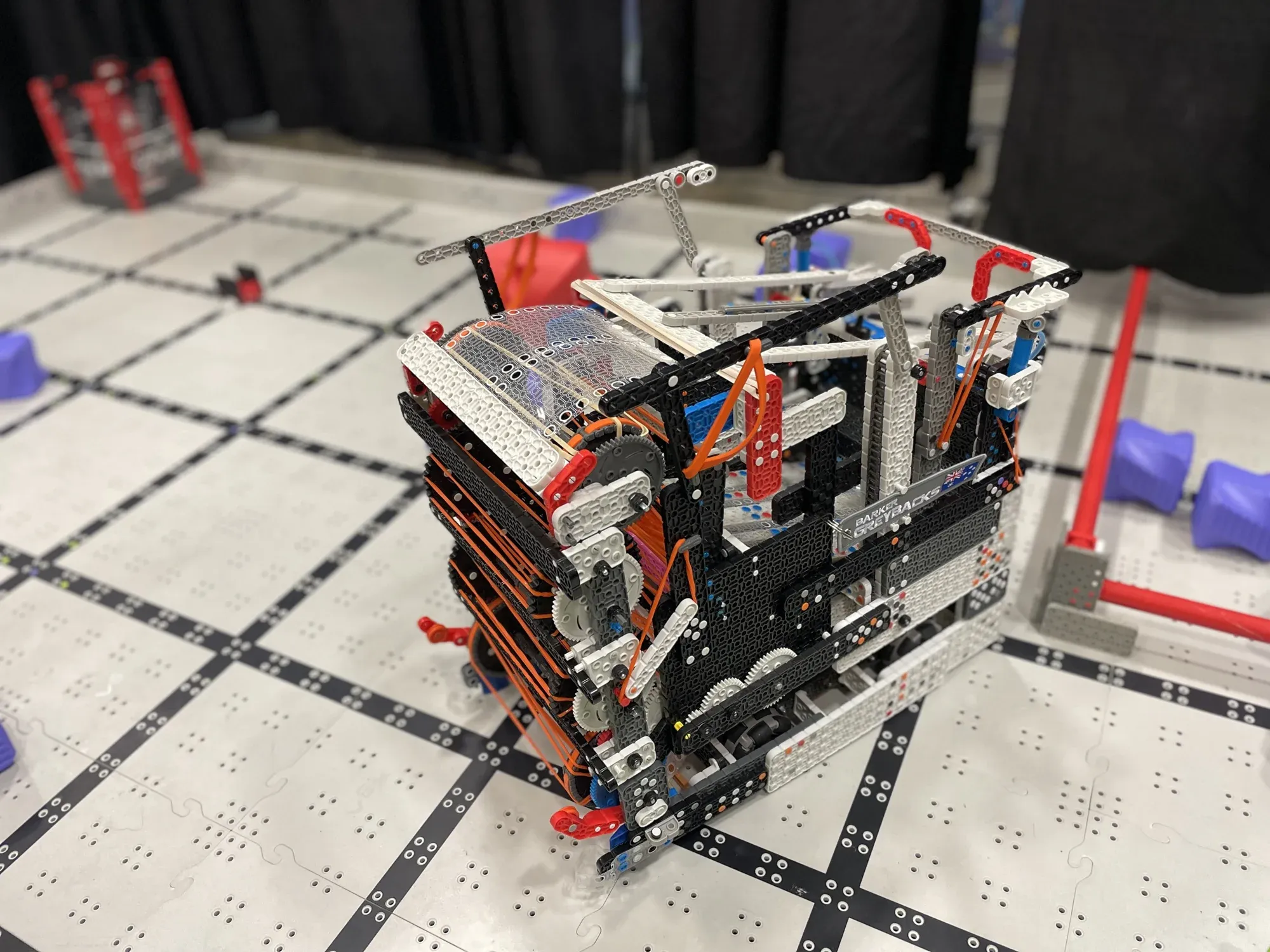 A black and white VEX IQ robot on a competition field with red field elements.