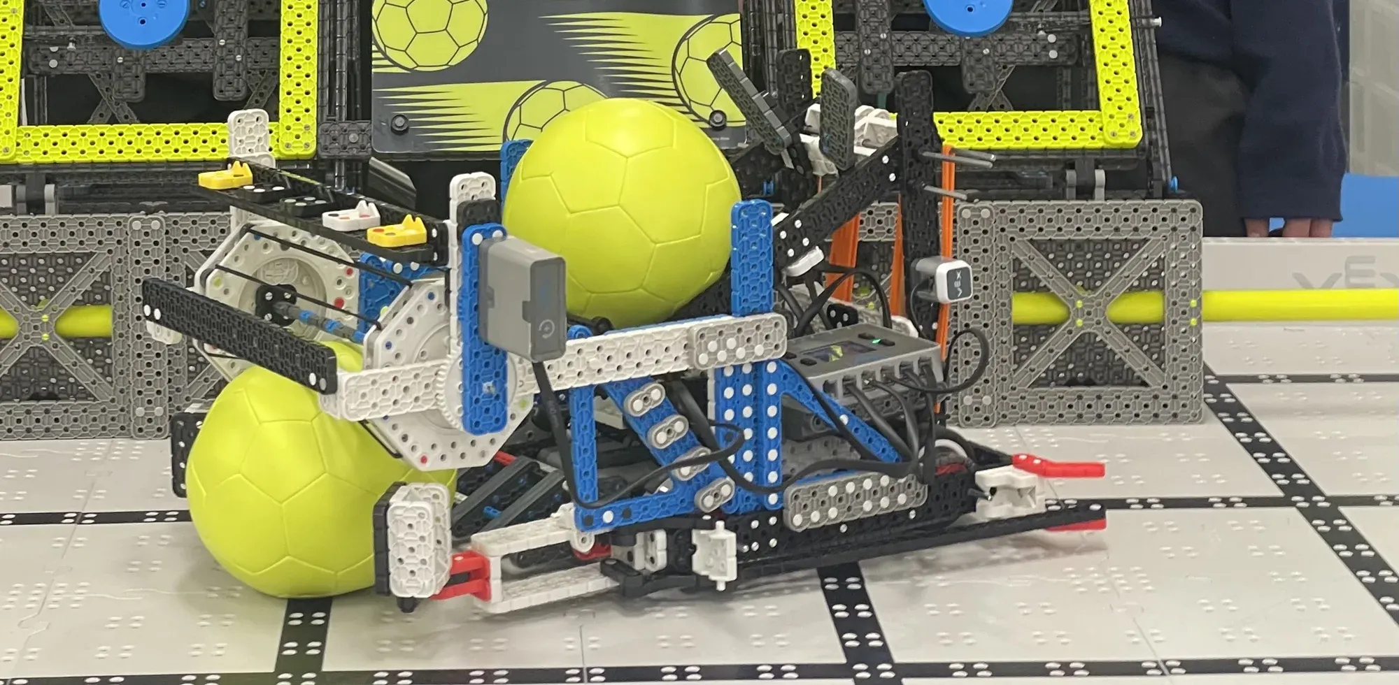 A VEX IQ robot holding two yellow balls on the field.