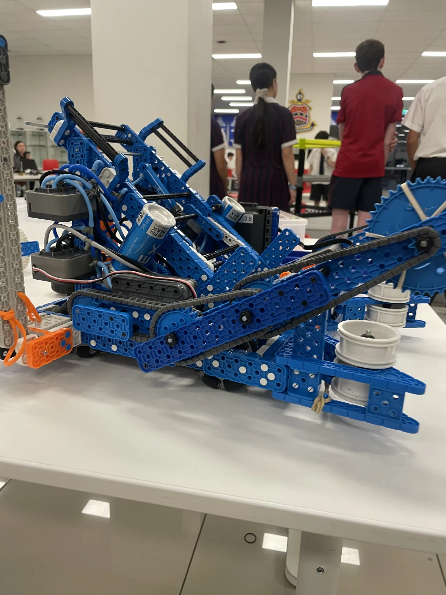 A blue VEX IQ robot with a tracked intake sitting on a table.