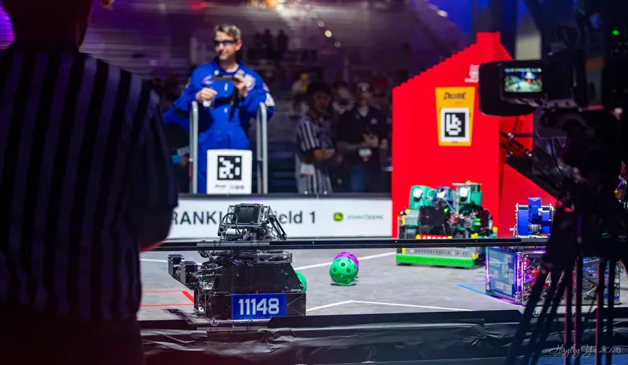 Robot 11148 on the field at the FIRST Championship in Houston, with a referee in the foreground and the DECODE goal behind.